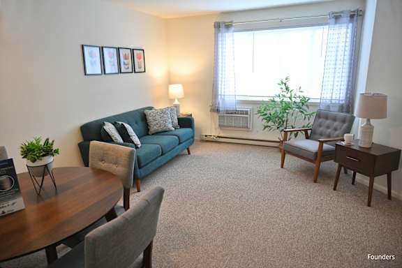 A living room with a blue couch, a grey armchair, a wooden table, and a carpet.