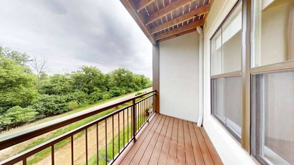 A balcony with a wooden floor and a railing overlooks a green landscape.