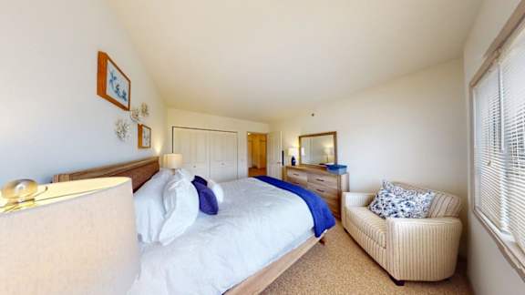 A bedroom with a bed, a chair, and a mirror.