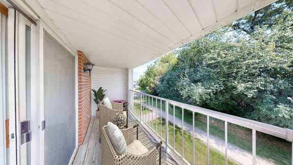 A balcony with a white railing and a wicker chair with a cushion.