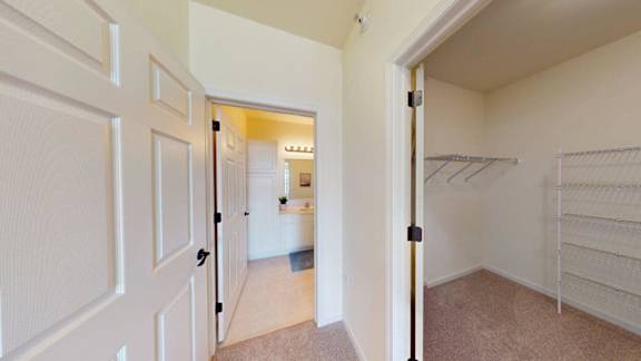 A white door opens to a hallway with a bedroom visible in the distance.