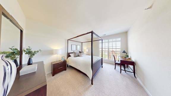 A bedroom with a four poster bed, a nightstand, a chair, and a plant.
