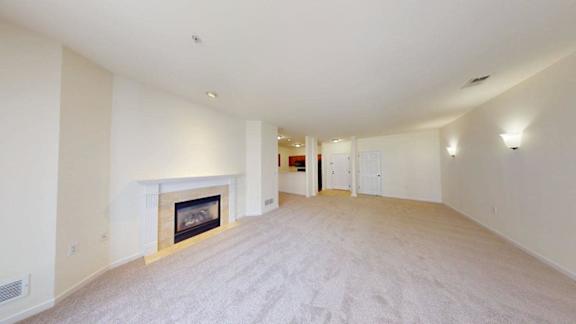 A large, empty room with a fireplace and carpeted floor.