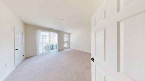 A room with white walls and a carpeted floor with a sliding glass door.