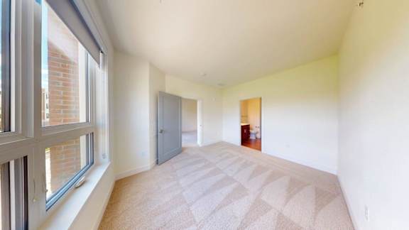 A room with a carpeted floor and a window on the left side.