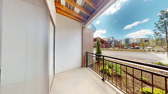 A balcony with a black railing and a view of a parking lot and buildings.