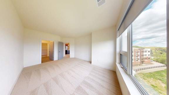 A large, empty room with a carpeted floor and a view of a building outside the window.