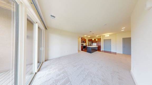 A spacious room with a carpeted floor and a table with chairs in the background.