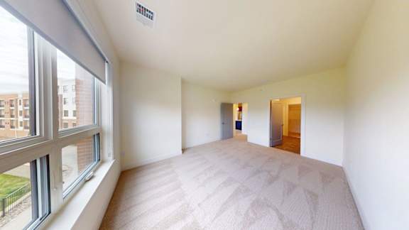 A large, empty room with a carpeted floor and a window overlooking a building.