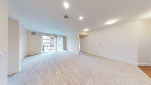 A spacious room with a carpeted floor and a window with a view of a balcony.