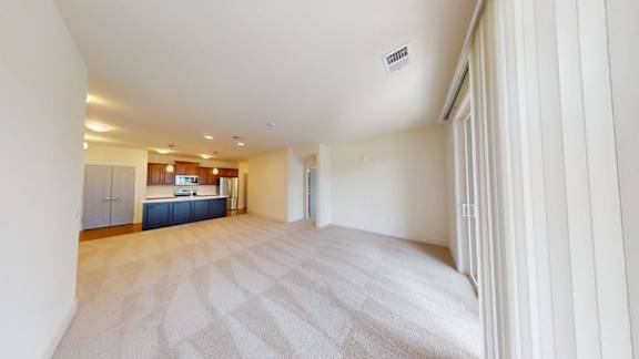 A spacious room with a carpeted floor and a kitchen area in the background.
