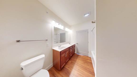 A white toilet sits in a small bathroom with a wooden vanity and medicine cabinet.