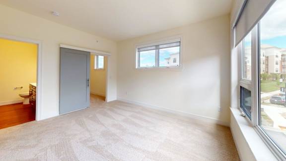 A room with a carpeted floor, a window, and a door.