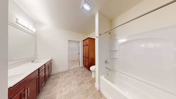 A bathroom with a white tub and wooden cabinets.