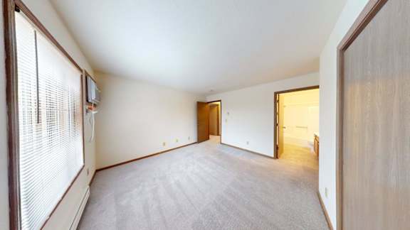 A room with a carpeted floor and a window with blinds.