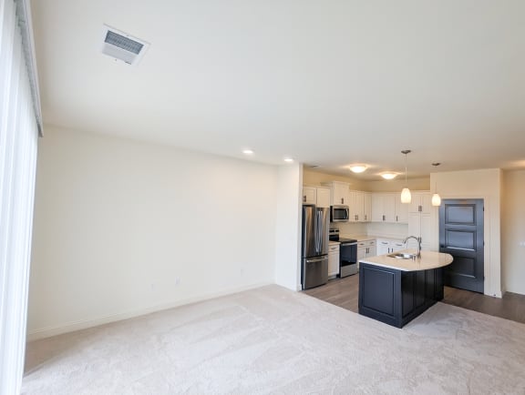 an empty living room with a kitchen with a sink and refrigerator