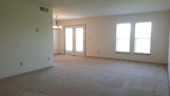 A room with a carpeted floor, a ceiling fan, and a door leading to another room.