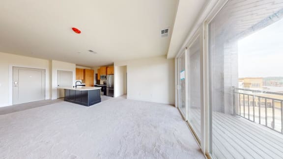 a large empty living room with a balcony and a kitchen