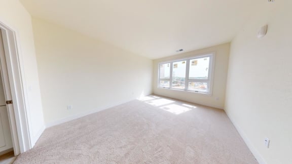 a spacious living room with a large window and carpet