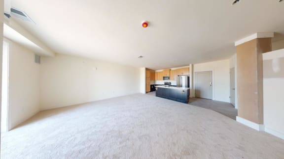 an empty living room with a kitchen in the background