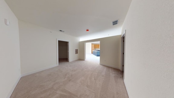 the living room and kitchen of an apartment with white walls and carpet
