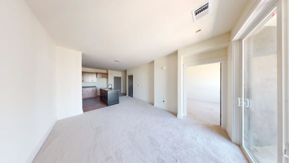 an empty living room with a kitchen in the background
