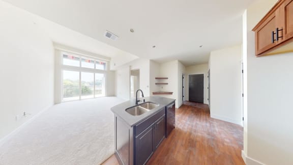 an empty living room with a kitchen with a sink