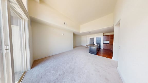 an empty living room with a kitchen in the background