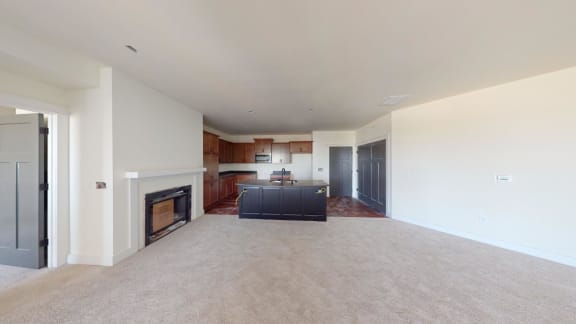 an empty living room with a fireplace and a kitchen
