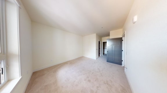 a spacious living room with white walls and carpeting and a blue door