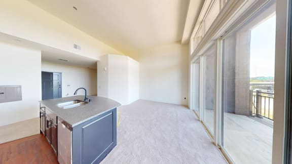 an empty living room with a kitchen and a large window