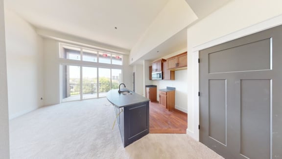 an empty living room with a kitchen and a door to a balcony