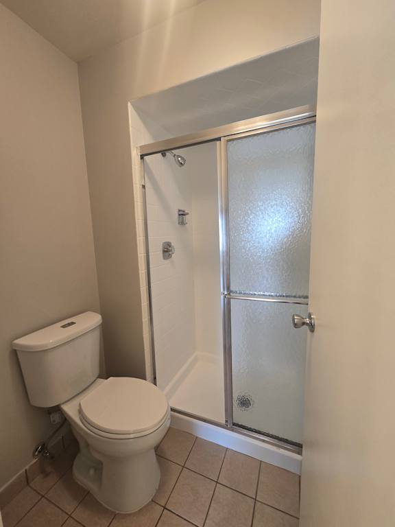 A white toilet with a toilet paper holder and a glass shower door.