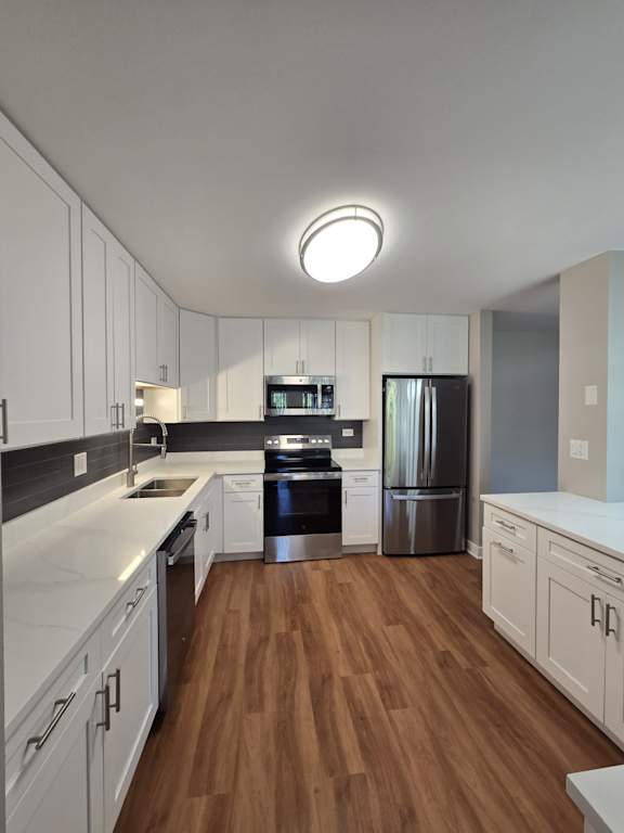 A modern kitchen with white cabinets and a wooden floor.
