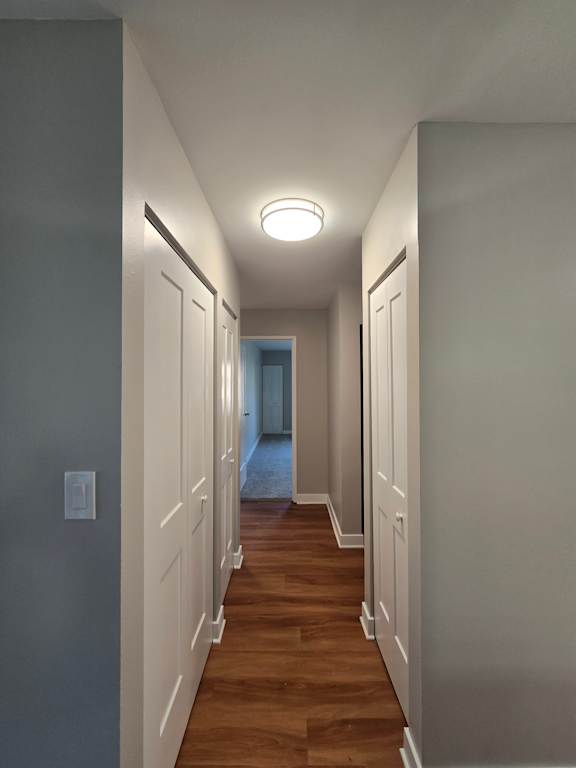 A long, narrow hallway with a light on the left side and a door at the end.