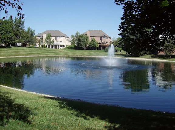 A fountain in the middle of a pond in front of a house.