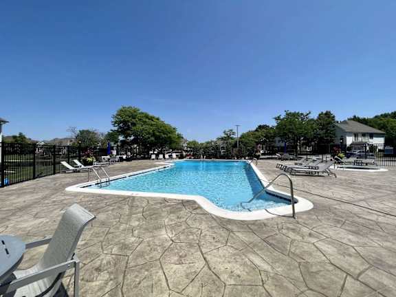 A pool surrounded by chairs and trees.