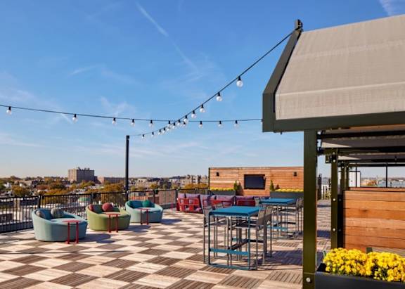 A rooftop patio with a checkerboard patterned floor, outdoor furniture, and string lights.