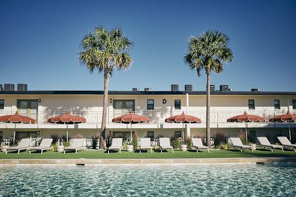 A hotel with a pool and palm trees in front.
