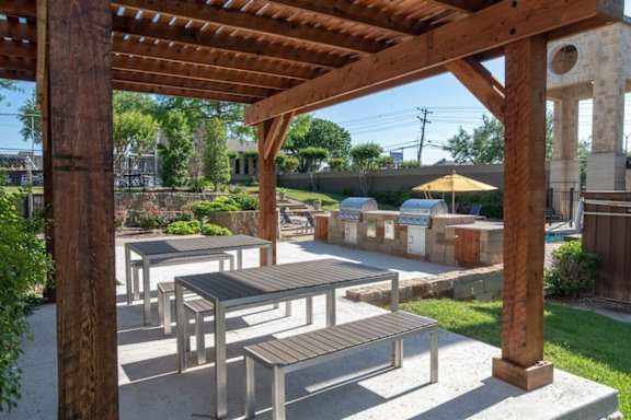 A wooden pergola with tables and benches is set up in a park.