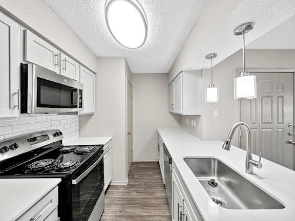 A kitchen with black and white appliances and a wooden floor.