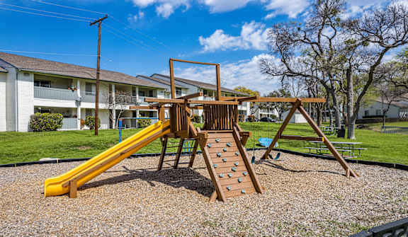A playground with a yellow slide and a wooden structure.