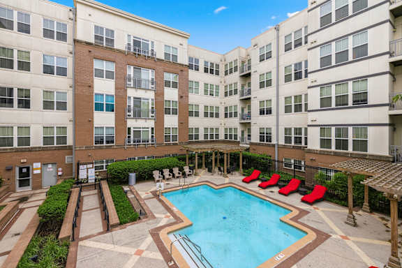 A large swimming pool surrounded by red chairs and apartment buildings.