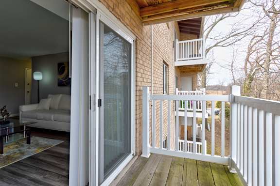 A balcony with a white railing and a glass door leading to a living room.