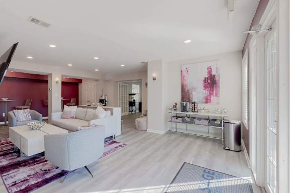 A modern living room with a white sofa set and a large painting on the wall.