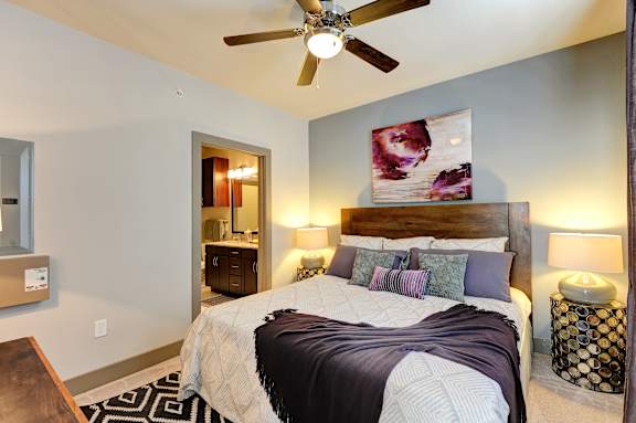 A bedroom with a bed, a ceiling fan, and a painting on the wall.