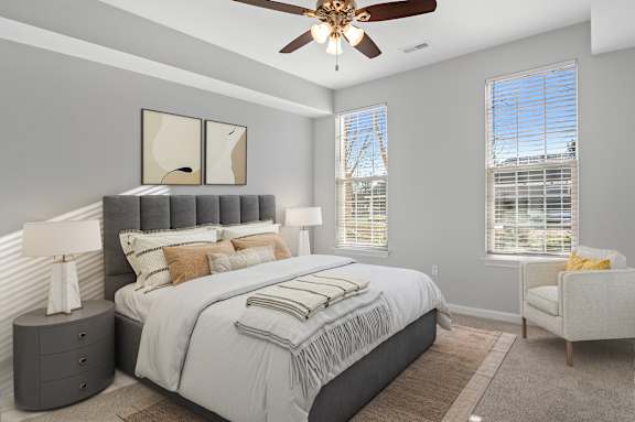 A bedroom with a large bed, a ceiling fan, and a chair.