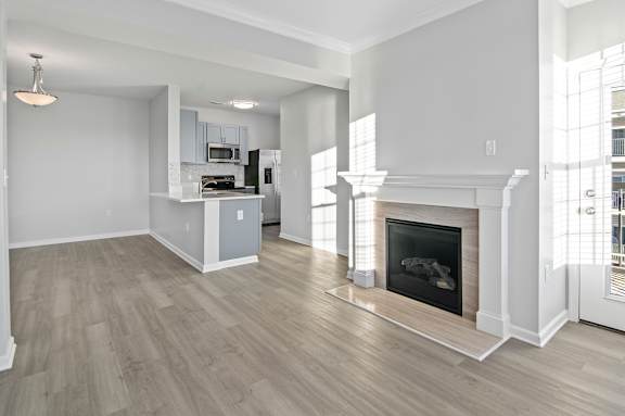 A large, empty living room with a fireplace and a kitchen area in the background.