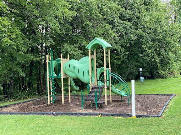 A playground with a green slide and a wooden structure.