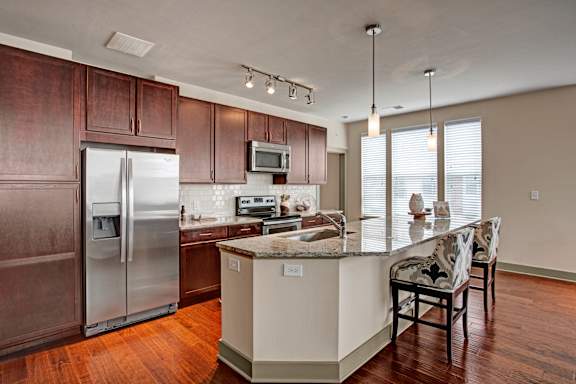 A kitchen with a refrigerator, microwave, and a counter with chairs.